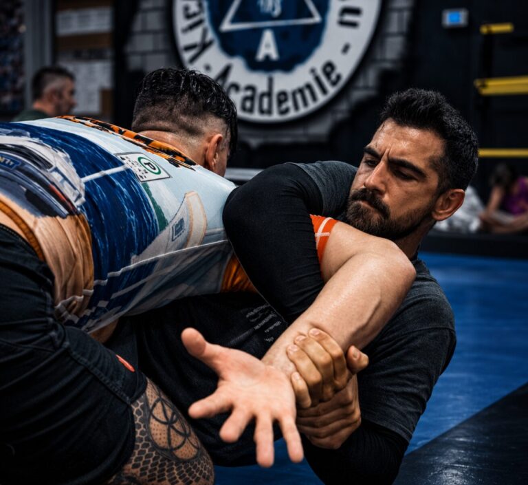 Deux athlètes s'entraînent au jiu-jitsu brésilien sans kimono (No-Gi) sur les tatamis de TEAM KJA, sous le logo circulaire de l'académie.