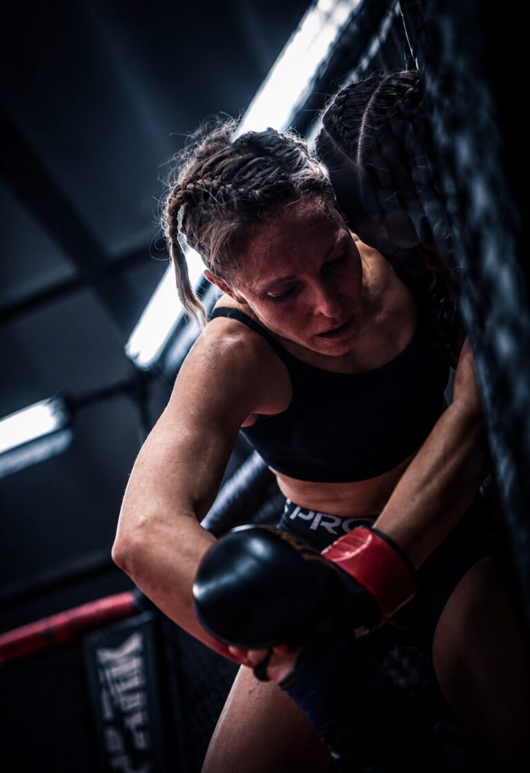 Athlète de TEAM KJA en entraînement MMA appuyée contre la cage
